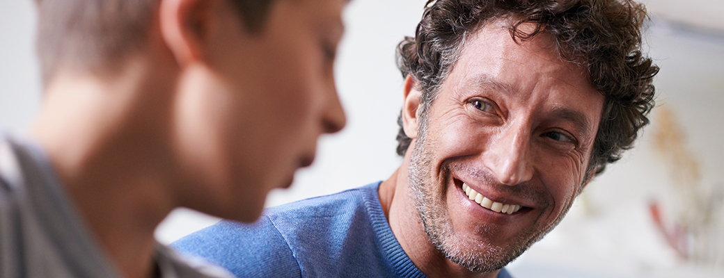 Image of man smiling and listening to a person talking beside them